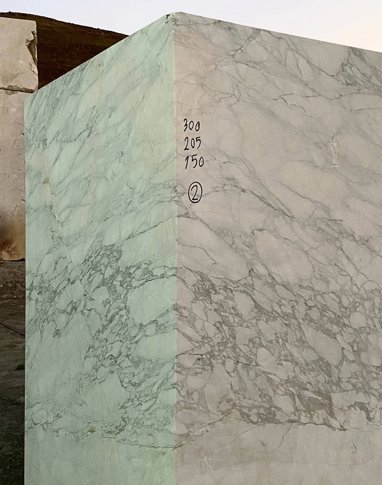 Photograph: a squared block of bright white stone with grey breccia-like veining at the quarry, hand-marked in black 300, 205 and 150 with a circled 2.