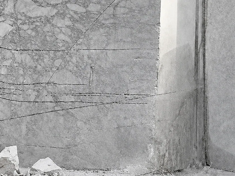 Photograph, close-up: wire-saw lines crossing the sawn face of a quarry bench, with broken stone at its foot.