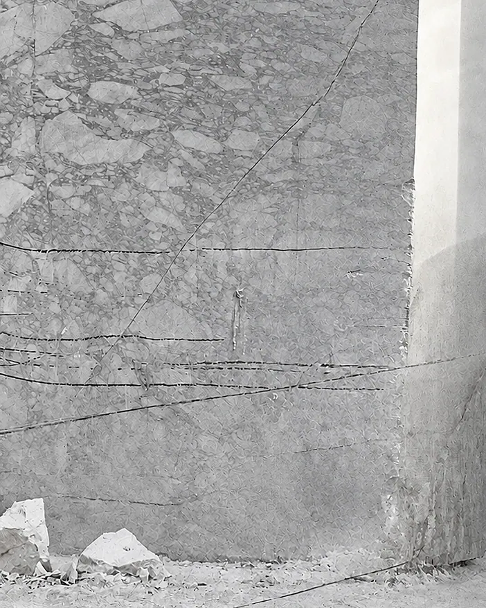 Photograph, close-up: wire-saw lines crossing the sawn face of a quarry bench, with broken stone at its foot.